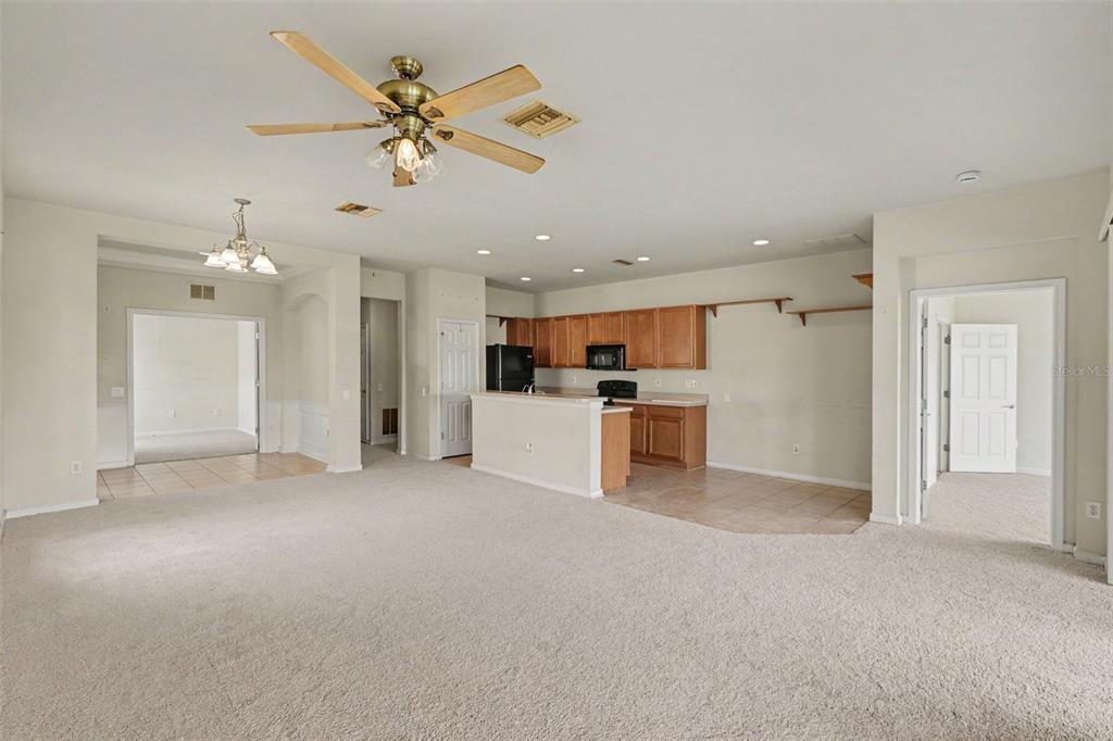 A spacious living room with beige carpet opens to a kitchen with wood cabinets — 13703 CREST LAKE DRIVE, HUDSON, FL