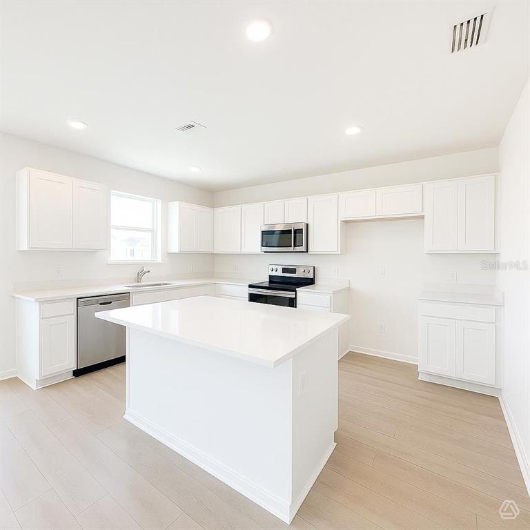 A modern kitchen features white cabinetry, a central island, and light wood-look flooring — 13213 SASSAFRAS TRAIL, PARRISH, FL
