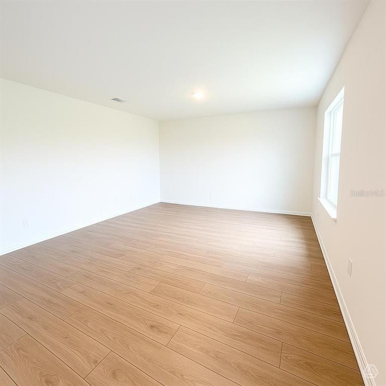 An empty room features light wood-look flooring, white walls, and a single window — 13213 SASSAFRAS TRAIL, PARRISH, FL