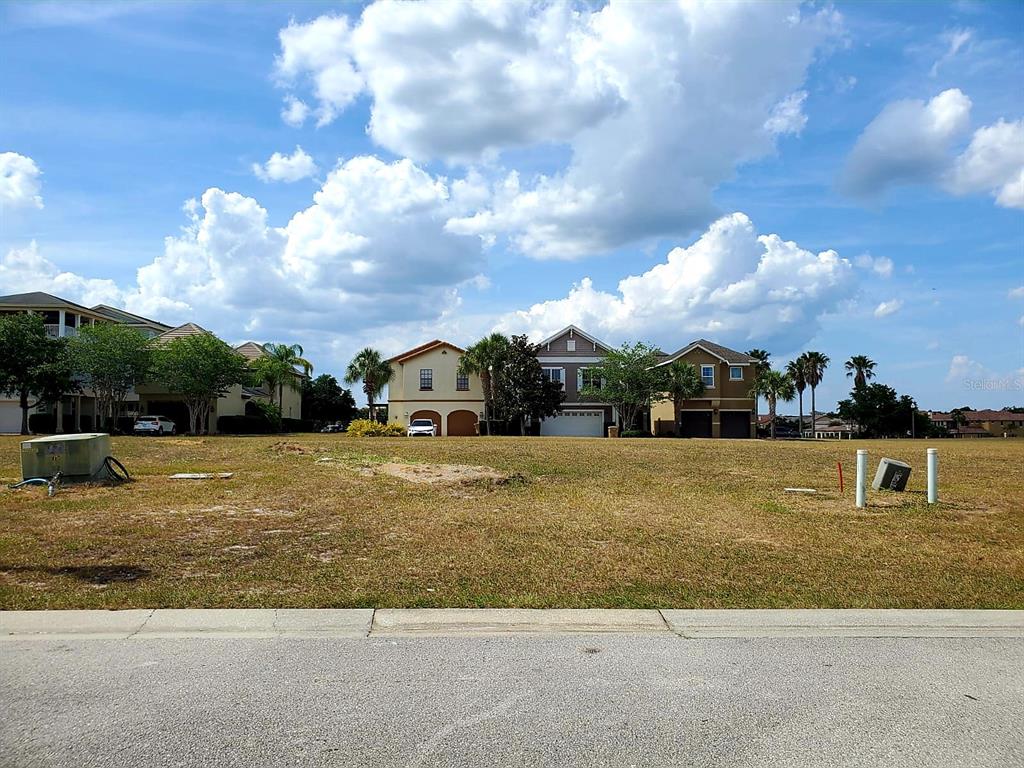 A vacant, grassy residential lot sits in front of several suburban houses under a cloudy sky — 7813 LOXAHATCHEE COURT, REUNION, FL
