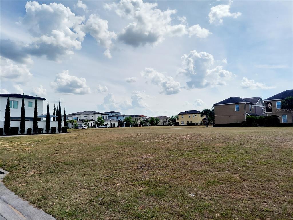 A large, vacant grassy lot is surrounded by suburban houses under a cloudy sky — 7813 LOXAHATCHEE COURT, REUNION, FL