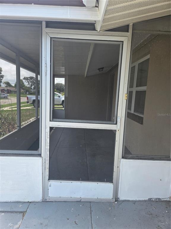 A screened-in porch with a white metal storm door and concrete flooring — 1731 DANDER DRIVE, HOLIDAY, FL