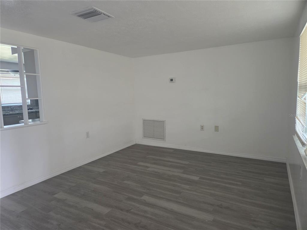 An empty room with white walls, gray wood-look flooring, and a window looking into a kitchen — 1731 DANDER DRIVE, HOLIDAY, FL