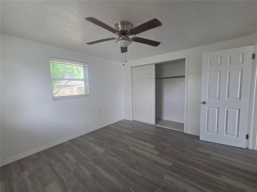 A bedroom with white walls, gray wood-look flooring, a ceiling fan, and a sliding closet — 1731 DANDER DRIVE, HOLIDAY, FL