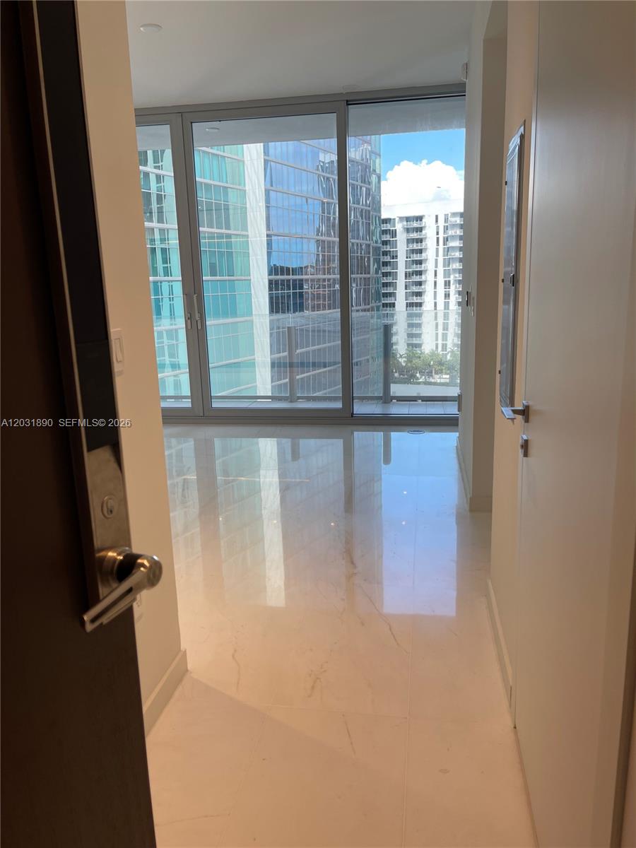 A hallway with white tile flooring leads to a glass door opening onto a balcony — 300 Biscayne Blvd Way # 2008, Miami FL 33131, MIAMI, FL
