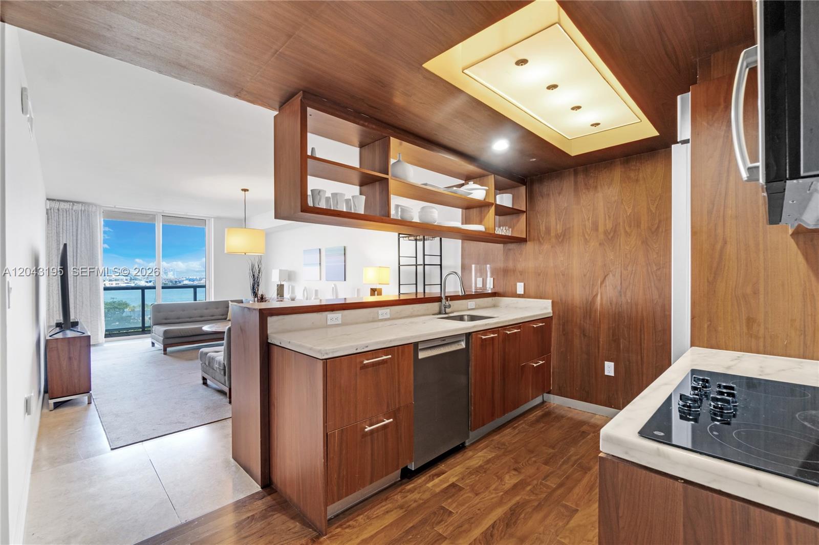 A modern kitchen features wood cabinetry, a marble countertop, and an open view of the living area — 50 Biscayne Blvd # 904, Miami FL 33132, MIAMI, FL