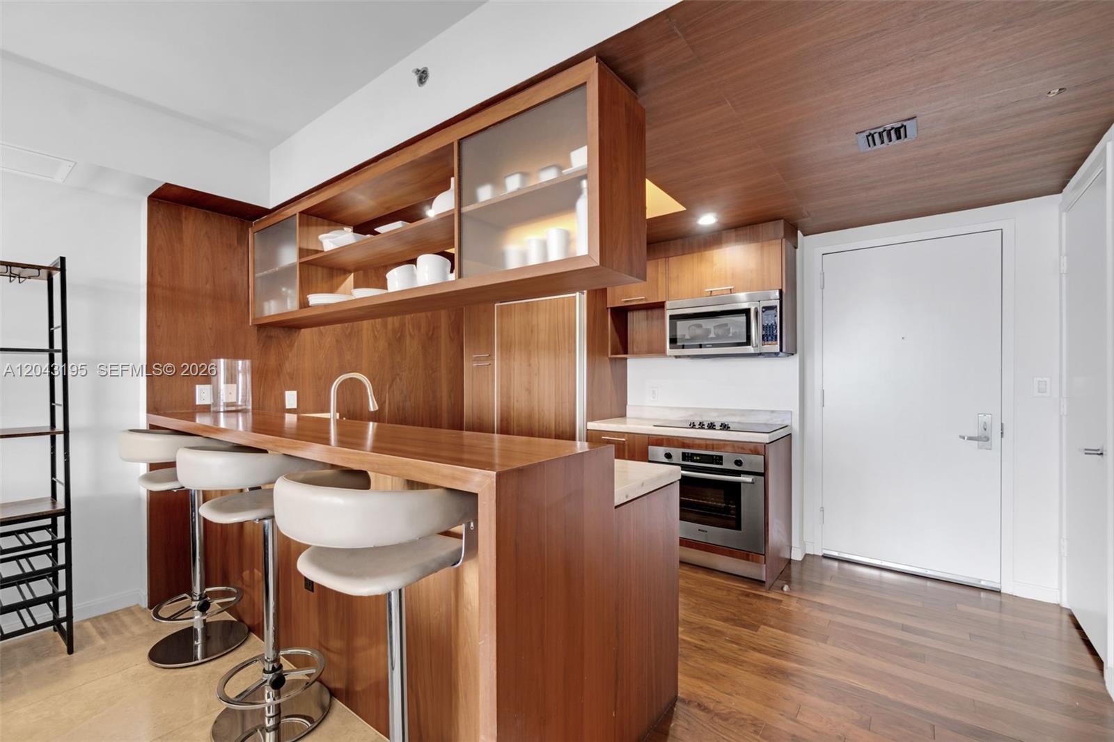 A modern kitchen features wood cabinetry, a breakfast bar with stools, and stainless steel appliances — 50 Biscayne Blvd # 904, Miami FL 33132, MIAMI, FL