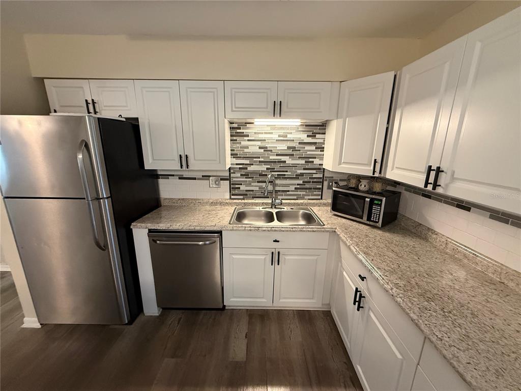 An open-concept living room and kitchen with wood-look flooring and white cabinetry — 5515 NW 27TH TERRACE, GAINESVILLE, FL
