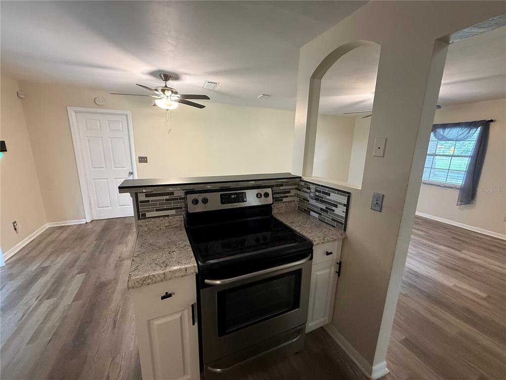 A kitchen features white cabinets, granite countertops, stainless steel appliances, and a gray tiled backsplash — 5515 NW 27TH TERRACE, GAINESVILLE, FL