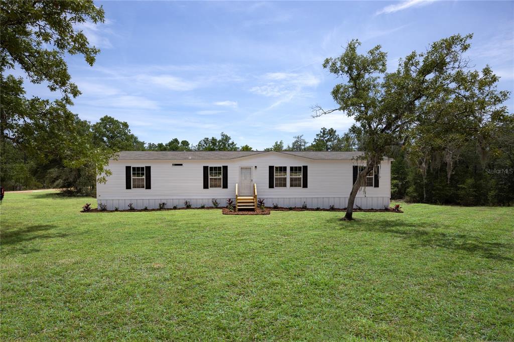 A single-story white manufactured home sits on a large, grassy lot with mature trees — 119 LONDON AVENUE, INTERLACHEN, FL