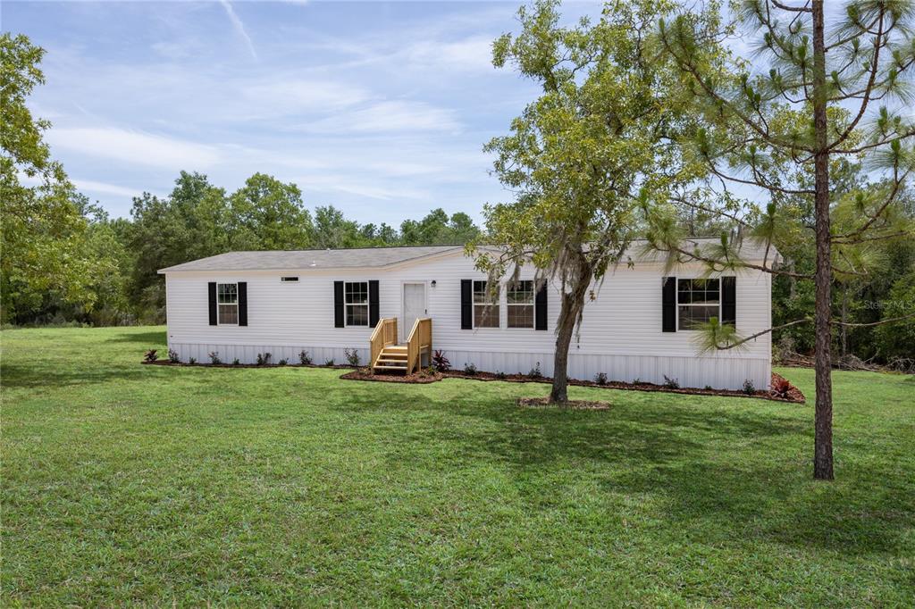 A white single-wide mobile home sits on a grassy lot surrounded by trees — 119 LONDON AVENUE, INTERLACHEN, FL