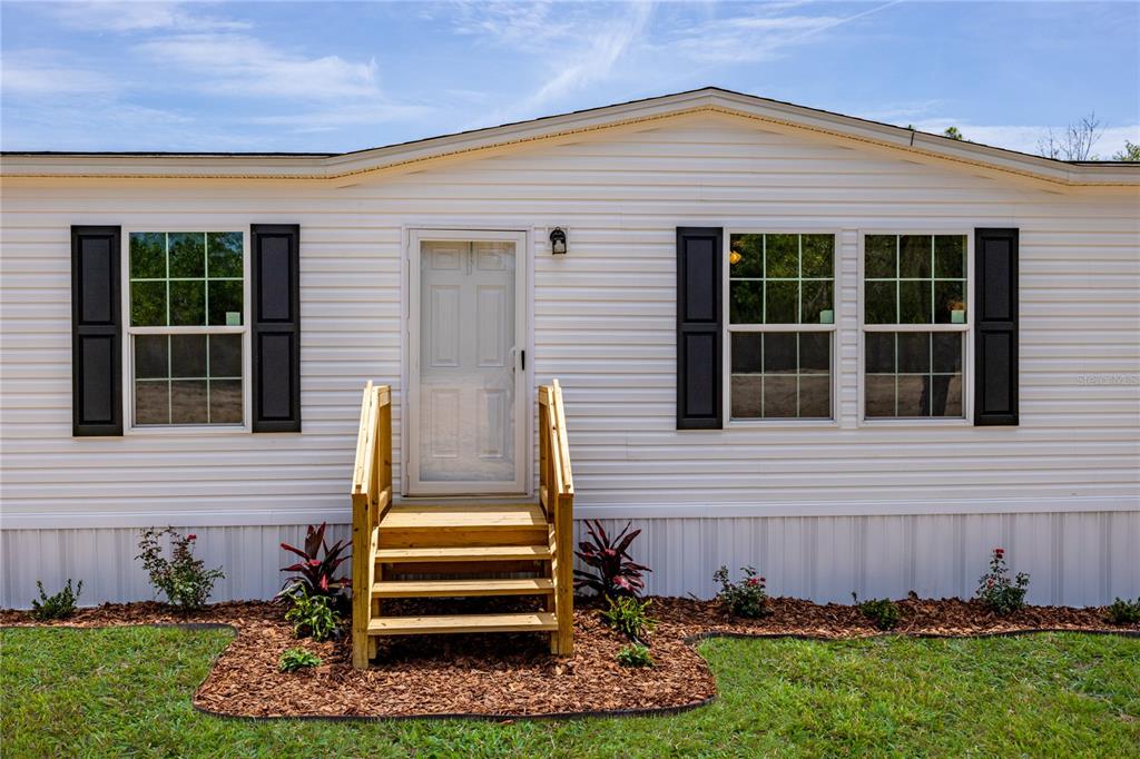 The exterior of a white mobile home features black shutters, a front door, and wooden steps — 119 LONDON AVENUE, INTERLACHEN, FL