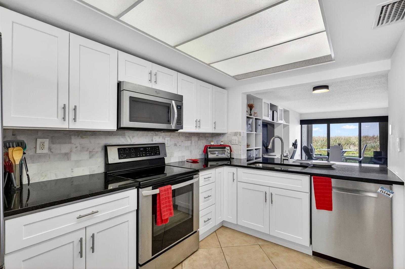 A kitchen with white cabinets, black countertops, stainless steel appliances, and a view of outdoors — 10310 S Ocean Drive # 107, Jensen Beach FL 34957, JENSEN BEACH, FL