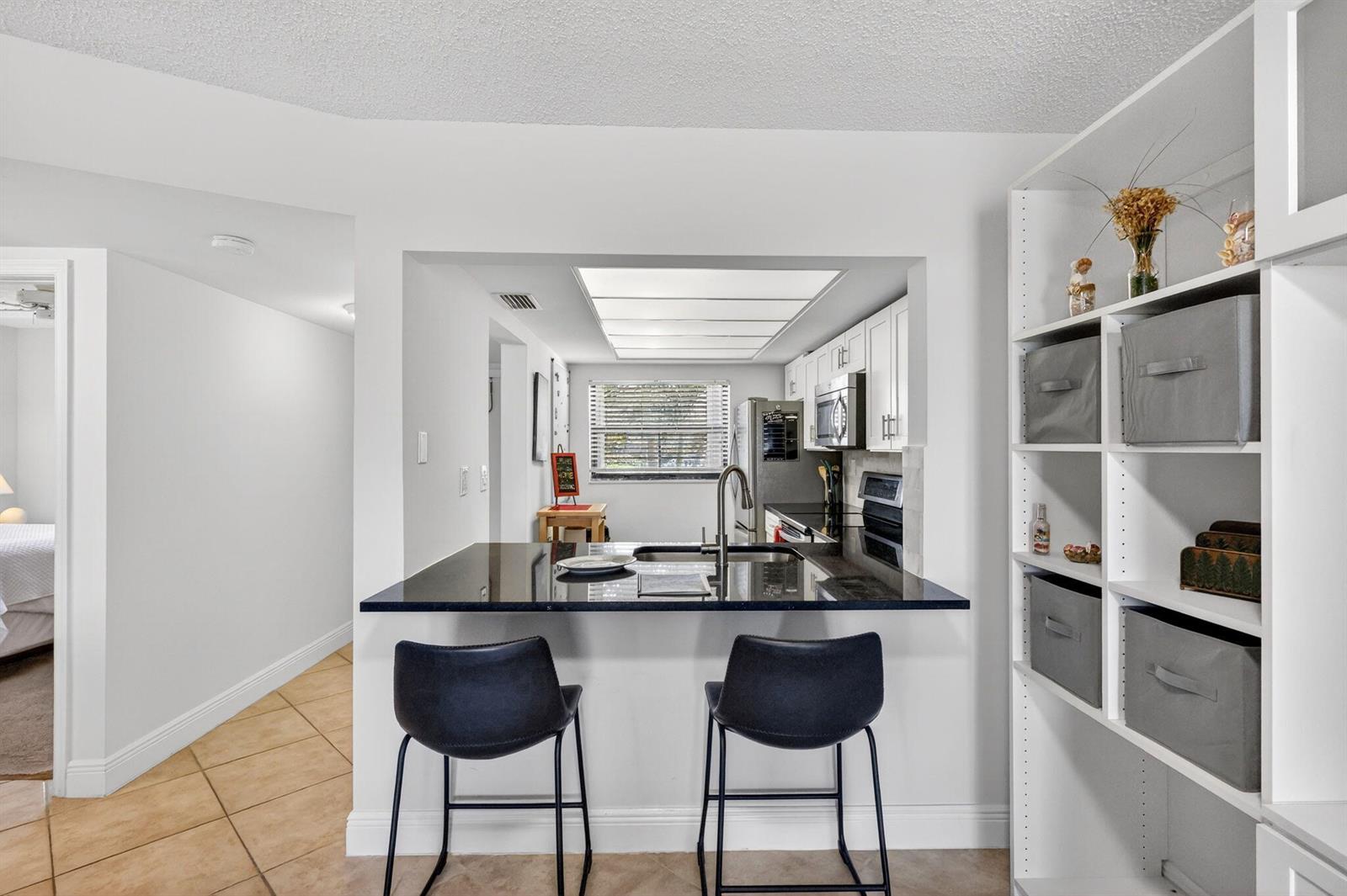 A kitchen with a black granite breakfast bar and two stools faces a white shelving unit — 10310 S Ocean Drive # 107, Jensen Beach FL 34957, JENSEN BEACH, FL