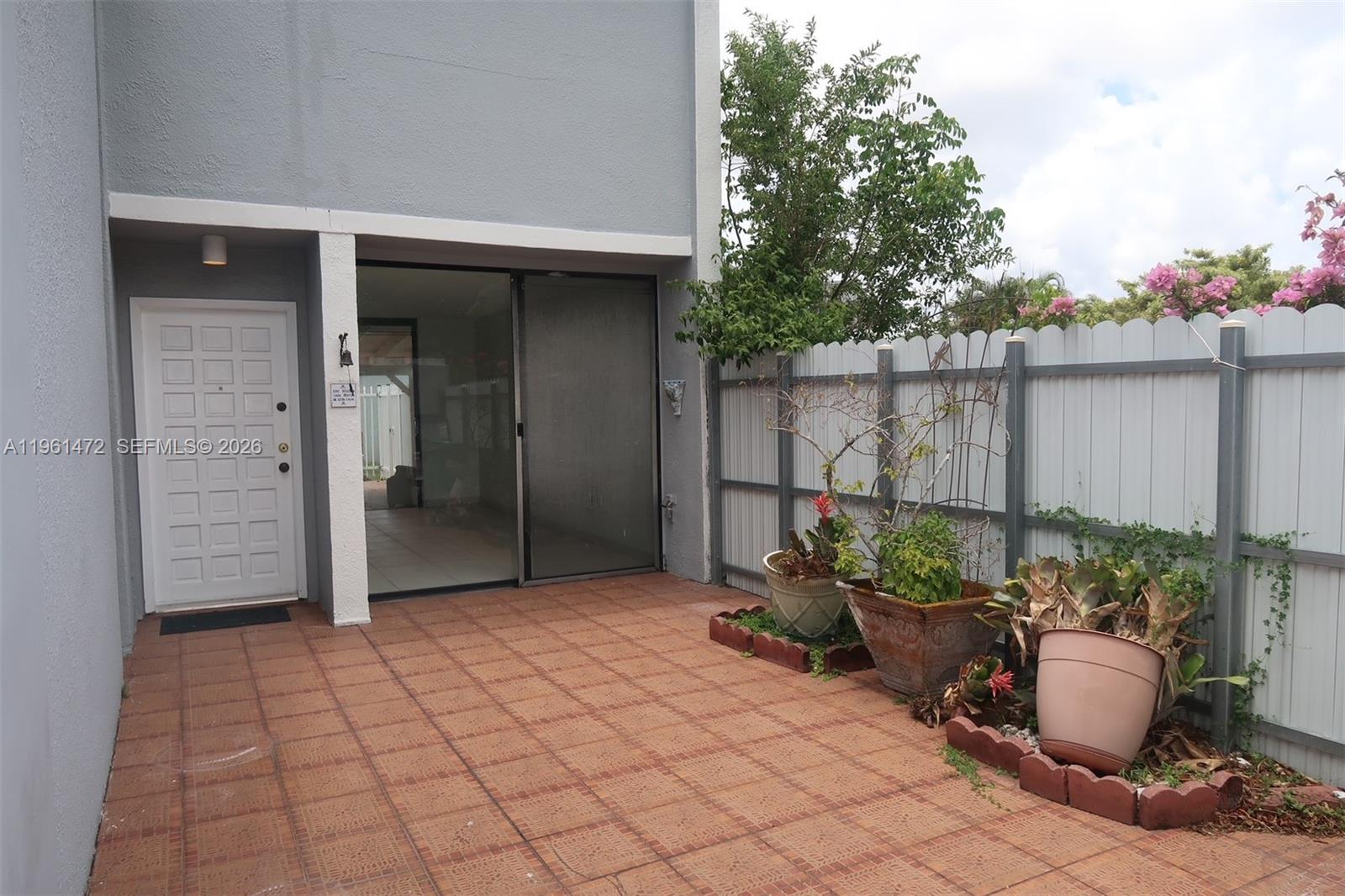A paved patio features potted plants and a white fence next to a sliding door — 2500 SW 122nd Ct, Miami FL 33175, MIAMI, FL