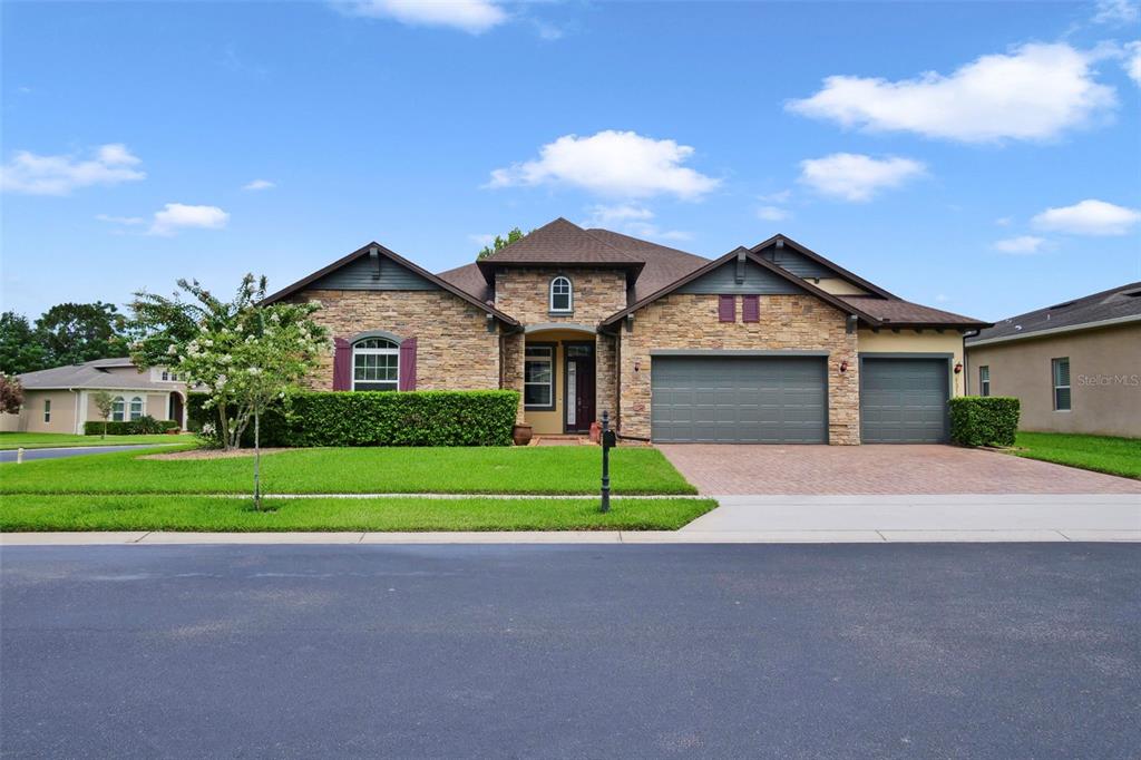 A single-story house with a stone facade, a three-car garage, and a manicured lawn — 1315 ARDEN OAKS DRIVE, OCOEE, FL