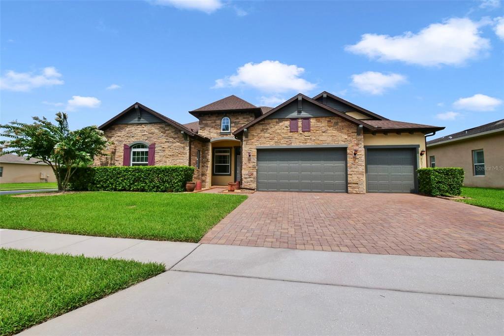 A stone-faced house with a three-car garage and a paved driveway under a blue sky — 1315 ARDEN OAKS DRIVE, OCOEE, FL