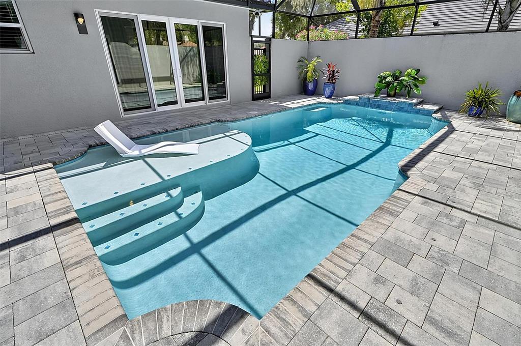 A swimming pool with a sun shelf and lounge chair sits on a paved patio — 38 NEW LEATHERWOOD DRIVE, PALM COAST, FL