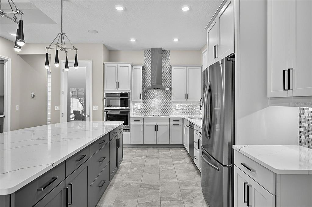 A modern kitchen features white and gray cabinetry, a large marble-topped island, and stainless steel appliances — 38 NEW LEATHERWOOD DRIVE, PALM COAST, FL