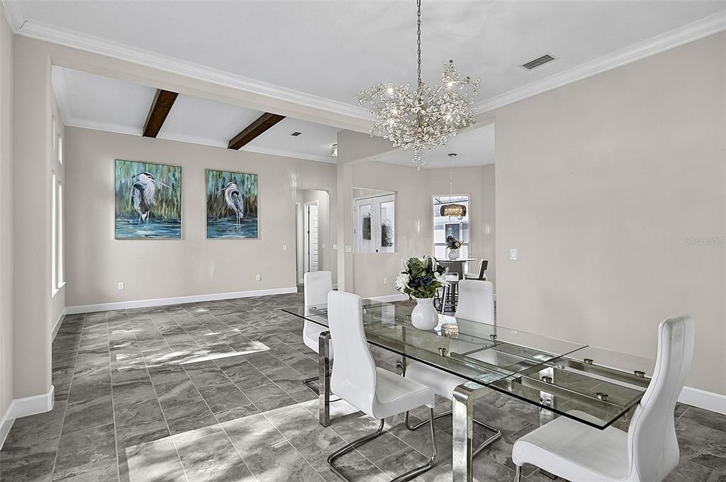 A dining room features a glass table, white chairs, a crystal chandelier, and tile flooring — 38 NEW LEATHERWOOD DRIVE, PALM COAST, FL