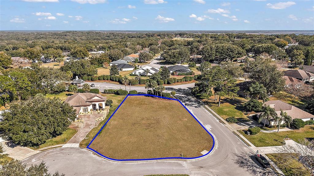 An aerial view shows a vacant, trapezoidal residential lot outlined in blue within a suburban neighborhood — 5049 HARBOR HEIGHTS, LADY LAKE, FL