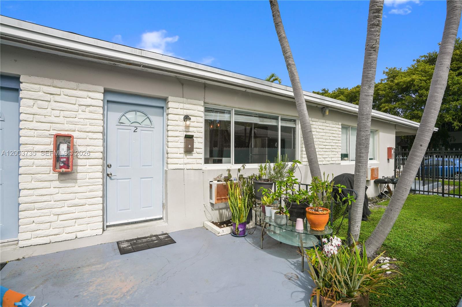 The exterior of a single-story building features a light blue door, white brick, and plants — 730 84th St, Miami Beach FL 33141, MIAMI BEACH, FL