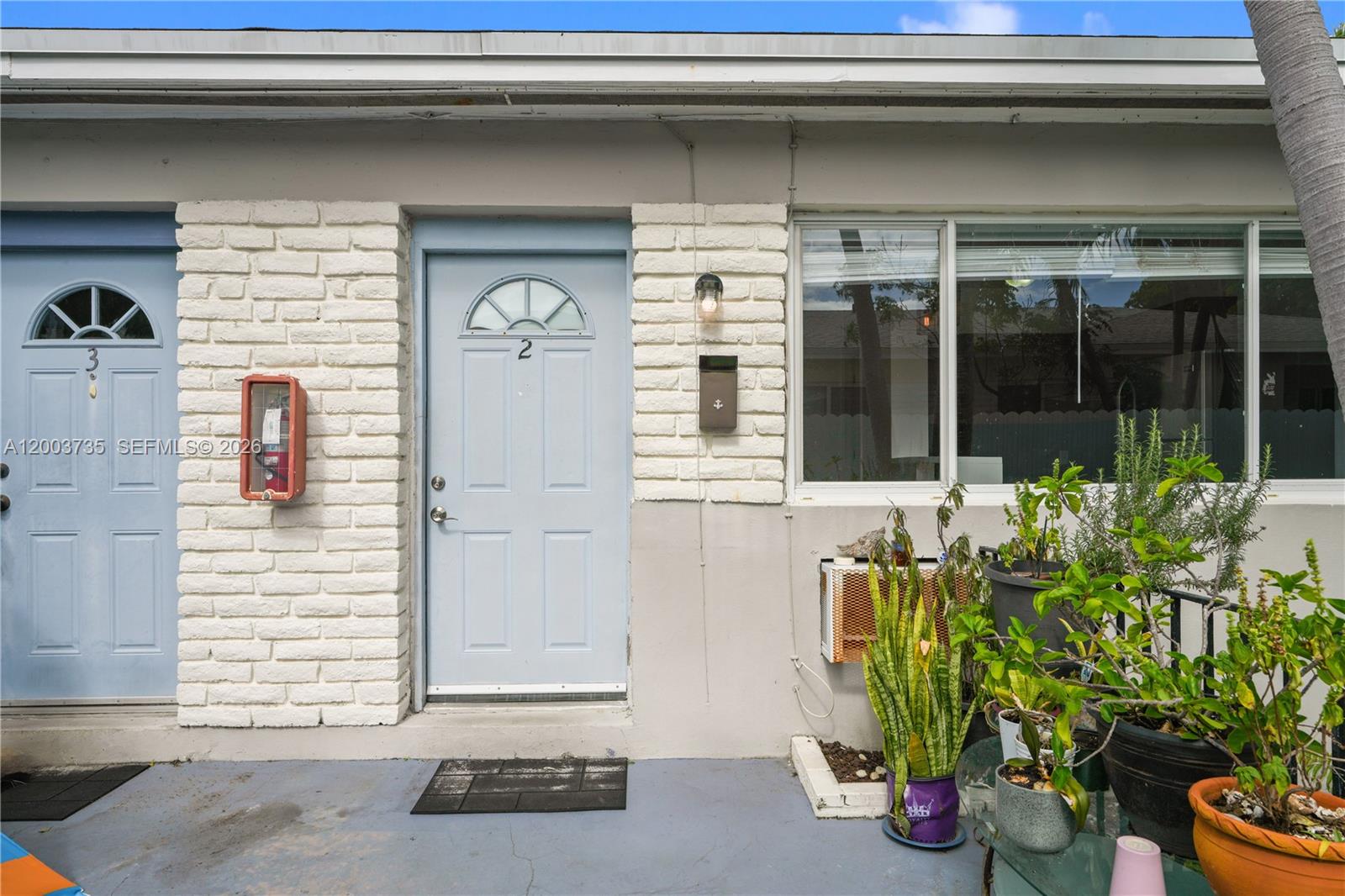The exterior view shows two light blue doors, white brick walls, and several potted plants — 730 84th St, Miami Beach FL 33141, MIAMI BEACH, FL