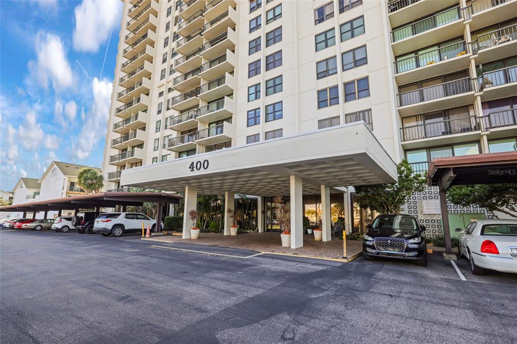 The exterior of a high-rise residential building features a covered entrance and parking area — 400 ISLAND WAY UNIT 602, CLEARWATER BEACH, FL
