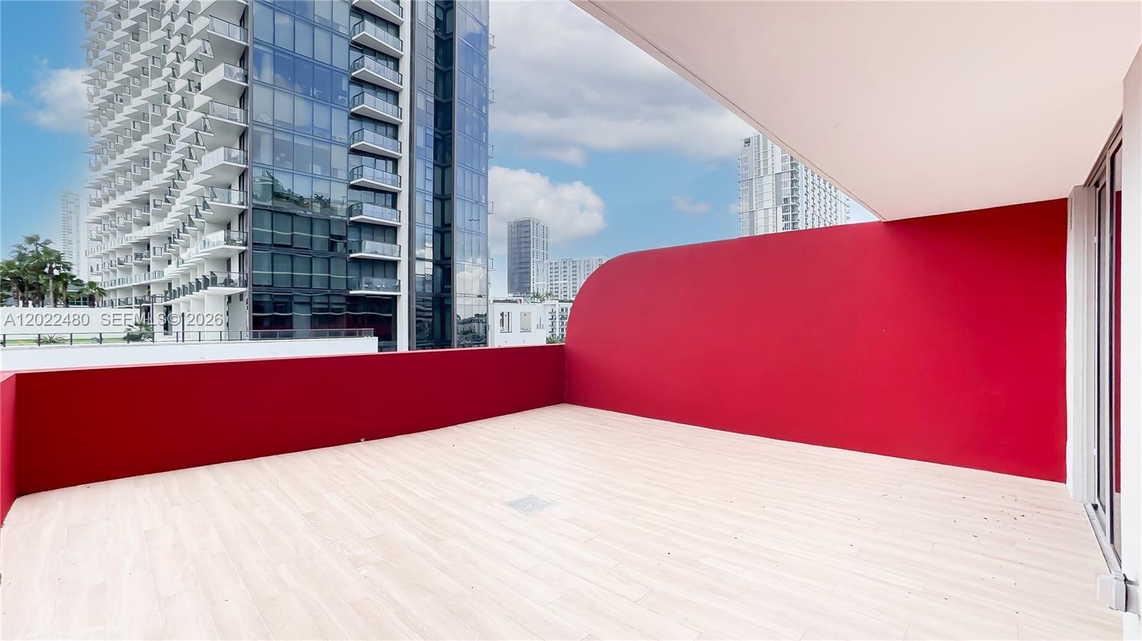 A spacious balcony features light wood-look flooring and a prominent curved red wall — 90 NE 32 # 608, Miami FL 33137, MIAMI, FL