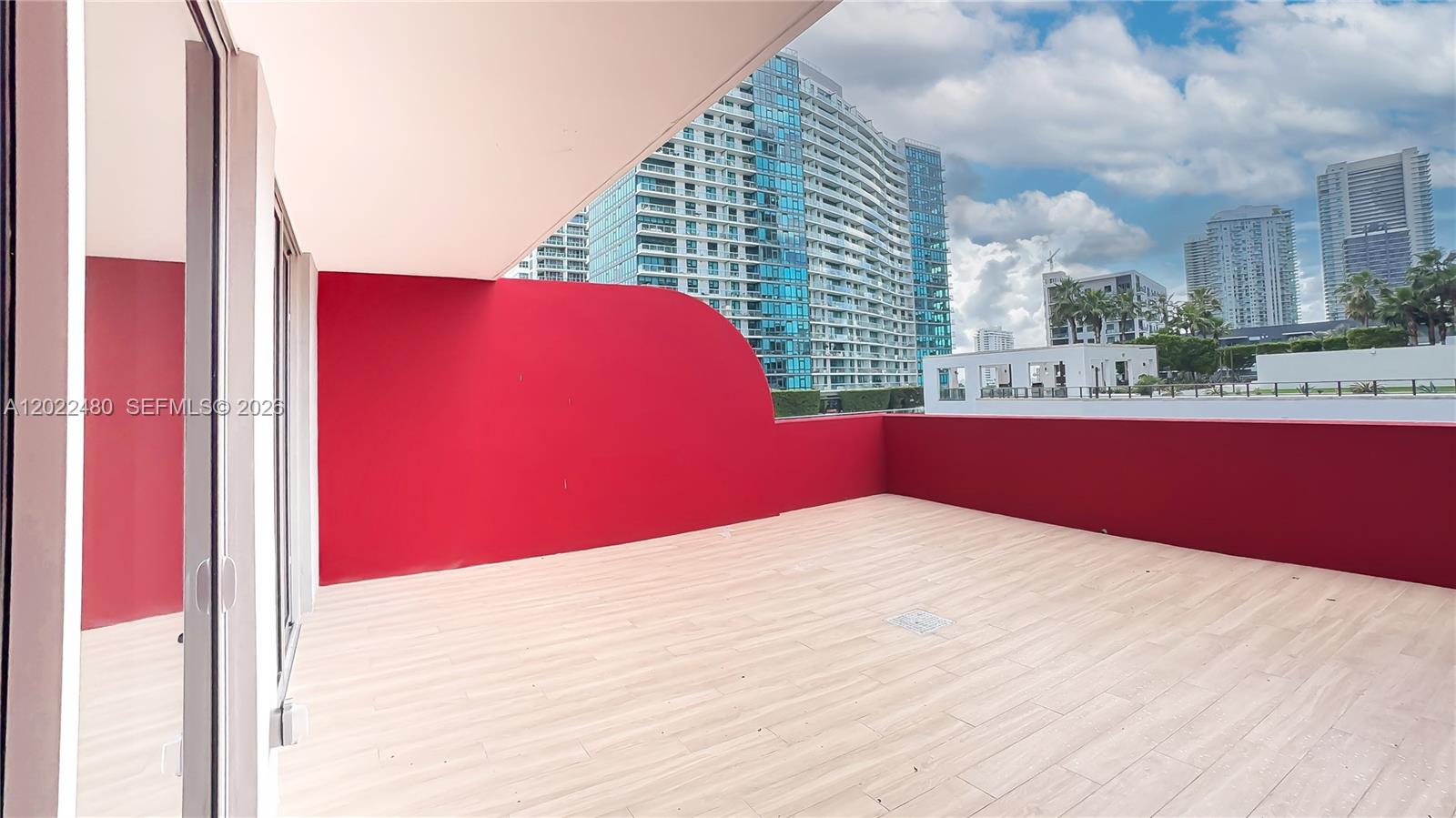 A spacious outdoor balcony features light wood-look tile flooring and a curved red wall — 90 NE 32 # 608, Miami FL 33137, MIAMI, FL