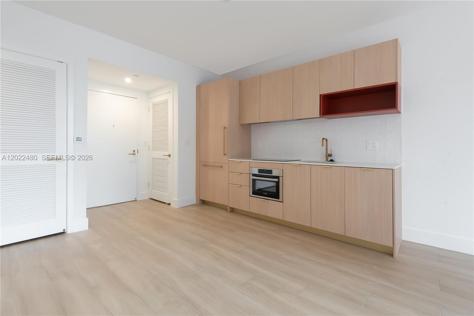 A modern kitchen features light wood cabinetry, a red open shelf, and white tile backsplash — 90 NE 32 # 608, Miami FL 33137, MIAMI, FL