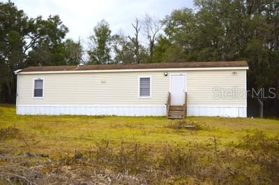 A single-story manufactured home with light-colored siding stands on a grassy lot near trees — 15731 SE 72ND PLACE, MORRISTON, FL