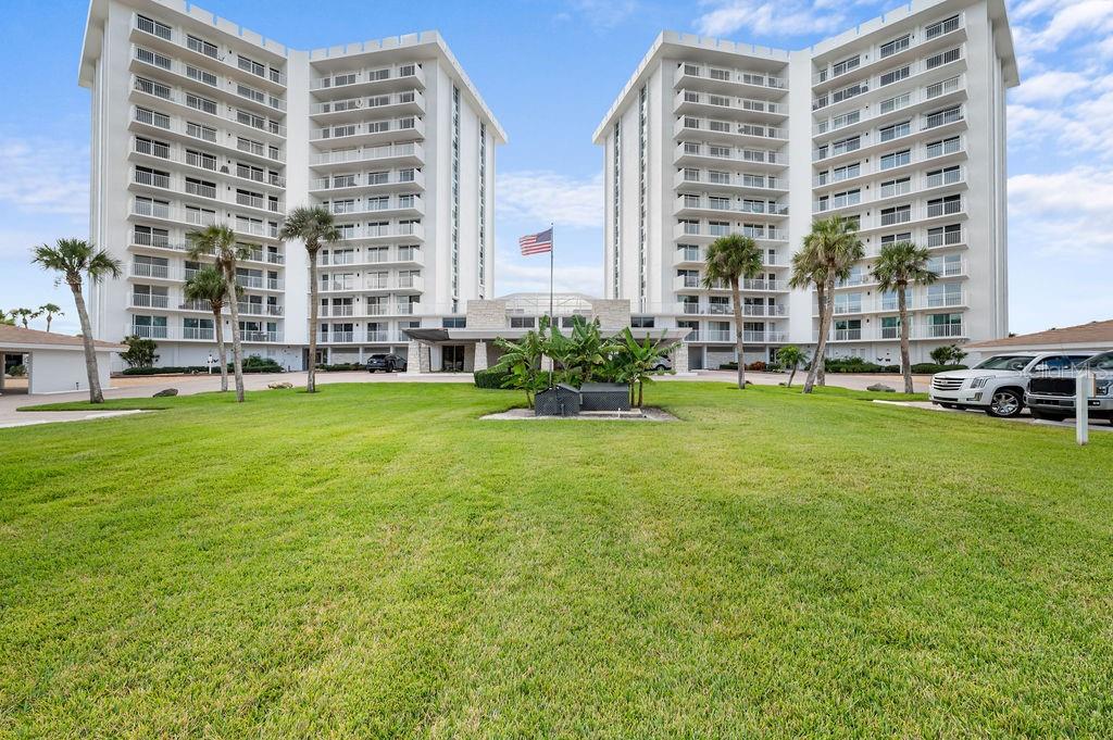 A large, multi-story white apartment complex stands behind a wide, manicured green lawn — 2295 GULF OF MEXICO DRIVE UNIT 54S, LONGBOAT KEY, FL