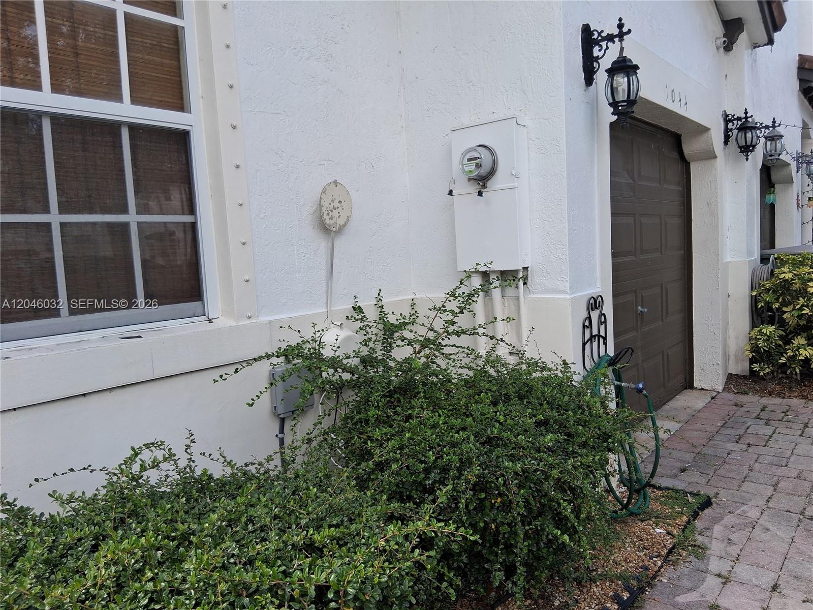 The exterior of a white building features a window, an electric meter, and landscaping — 1044 NE 30th Ave, Homestead FL 33033, HOMESTEAD, FL