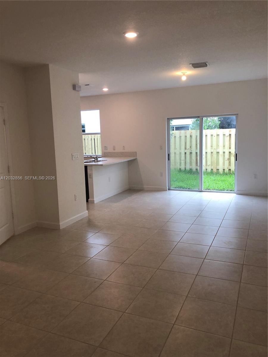 An open-concept living area features tile flooring, a kitchen breakfast bar, and sliding glass doors — 2610 SE 13th St, Homestead FL 33035, HOMESTEAD, FL