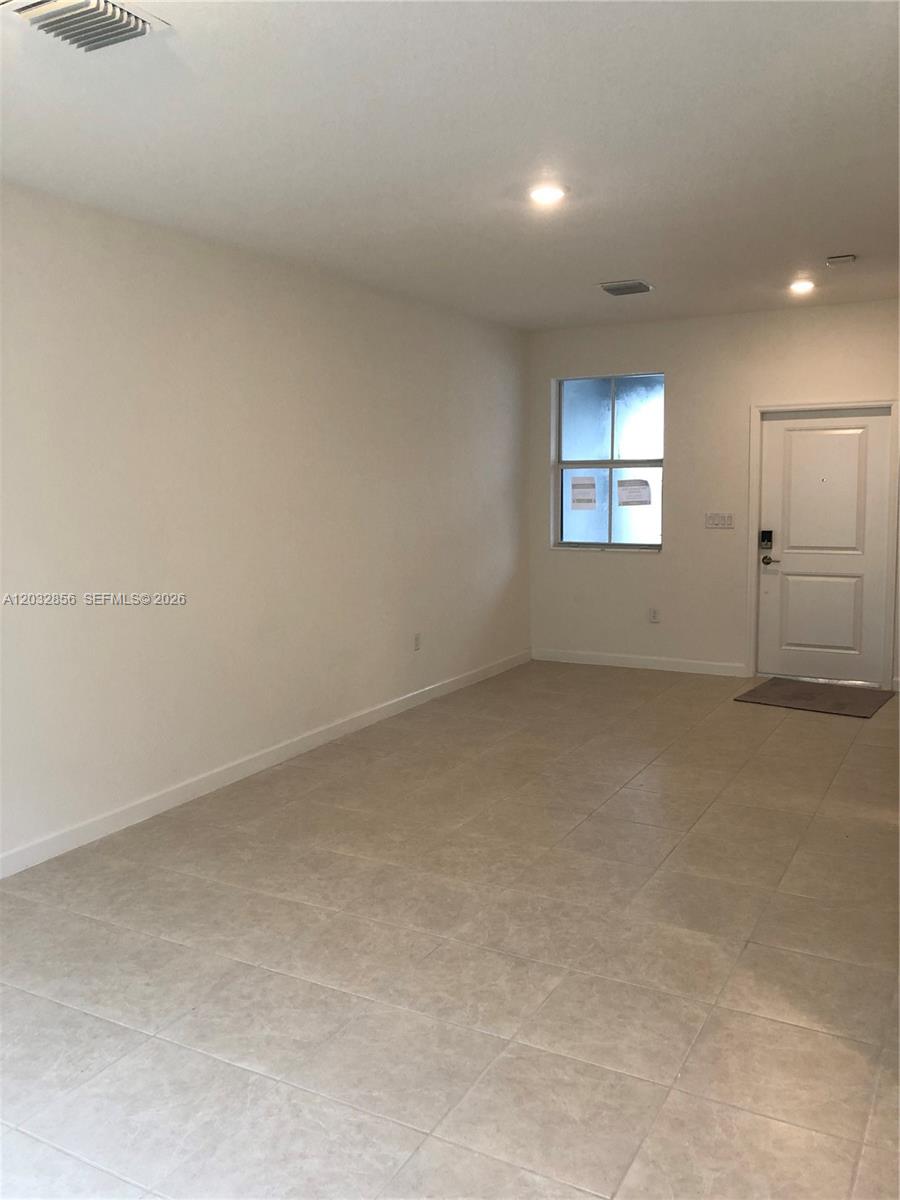 An empty room features light-colored tile flooring, white walls, a window, and a white door — 2610 SE 13th St, Homestead FL 33035, HOMESTEAD, FL