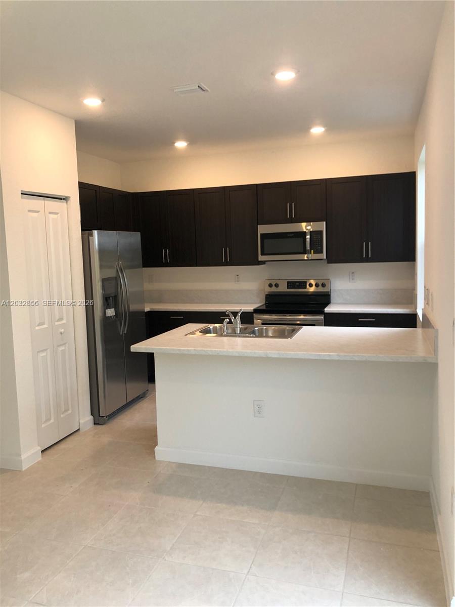 A kitchen features dark wood cabinets, stainless steel appliances, and a white countertop island — 2610 SE 13th St, Homestead FL 33035, HOMESTEAD, FL