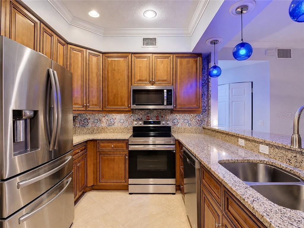 A kitchen with wooden cabinets, stainless steel appliances, granite countertops, and a patterned tile backsplash — 1051 WINDING PINES CIRCLE UNIT 105, CAPE CORAL, FL