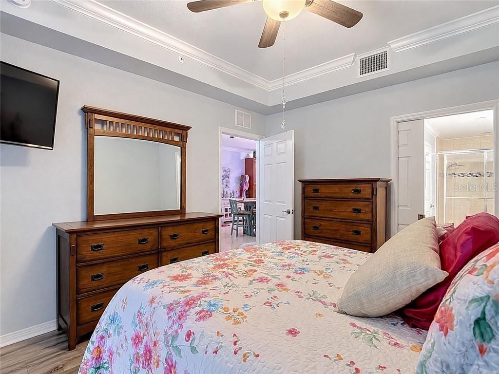 A bedroom features a floral bedspread, wooden dresser with a mirror, and a ceiling fan — 1051 WINDING PINES CIRCLE UNIT 105, CAPE CORAL, FL