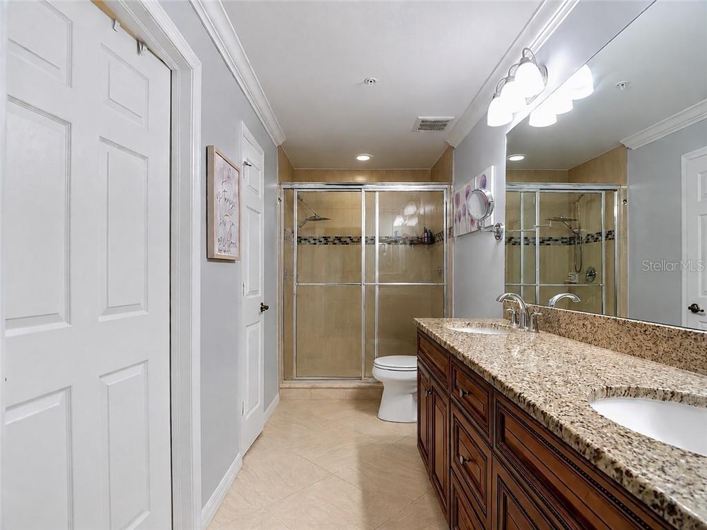 A bathroom features a double vanity with granite countertops, a walk-in shower, and tile flooring — 1051 WINDING PINES CIRCLE UNIT 105, CAPE CORAL, FL