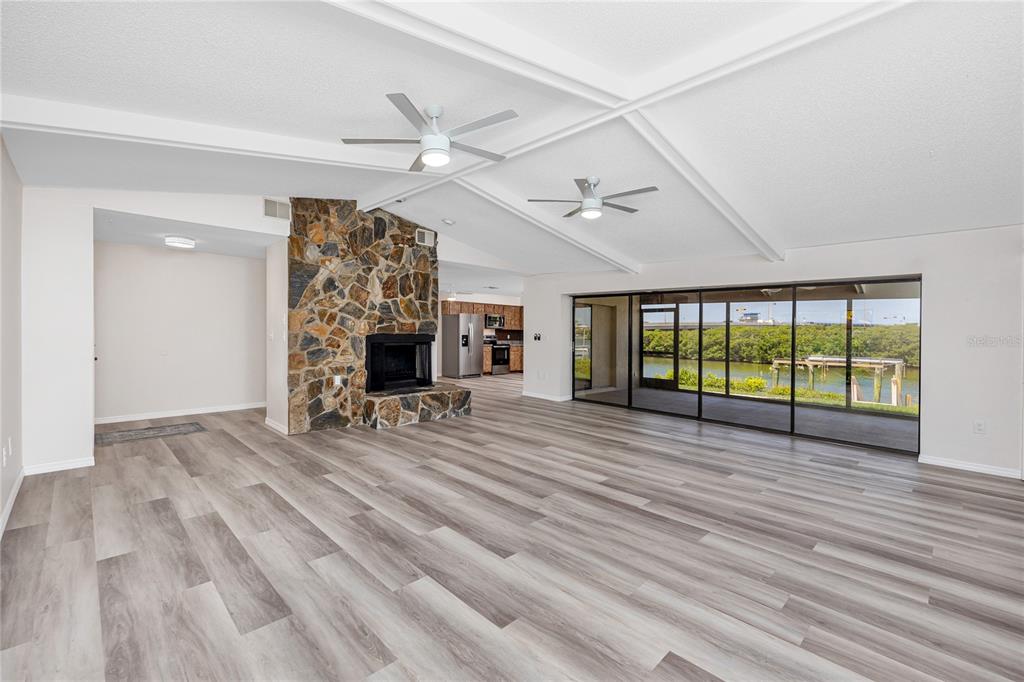 A spacious living room features a stone fireplace, light wood-look flooring, and large sliding glass doors — 8046 BAYHAVEN DRIVE, SEMINOLE, FL