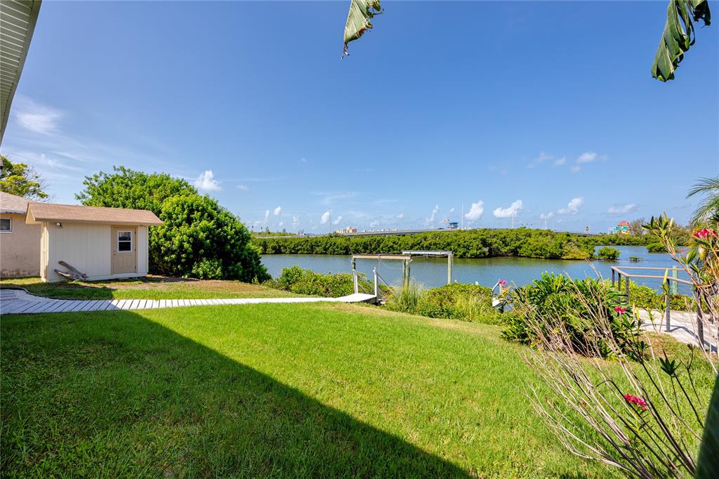 A grassy backyard features a small shed, a wooden walkway, and a view of water — 8046 BAYHAVEN DRIVE, SEMINOLE, FL