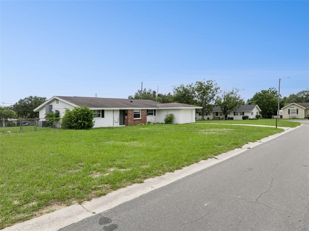 A single-story white house with a brick accent wall sits on a large grassy lot — 702 WILDABON AVENUE, LAKE WALES, FL