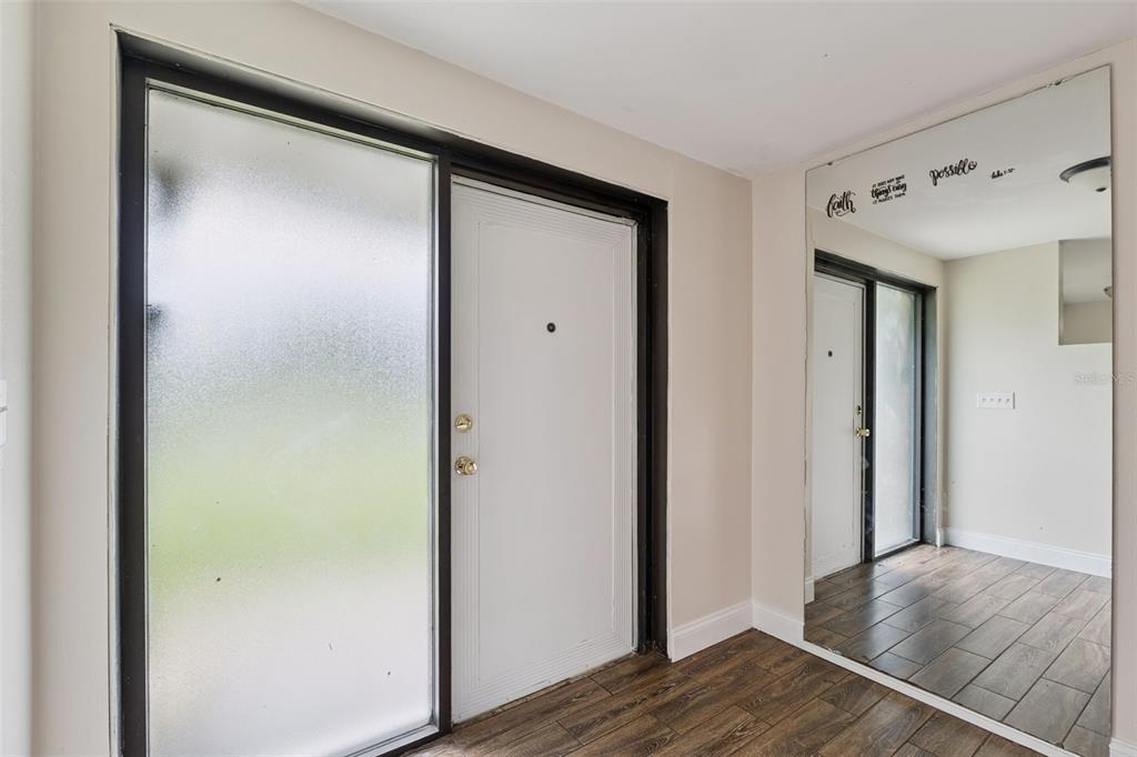 An entryway features a white front door with a frosted sidelight, wood-look flooring, and mirrors — 702 WILDABON AVENUE, LAKE WALES, FL