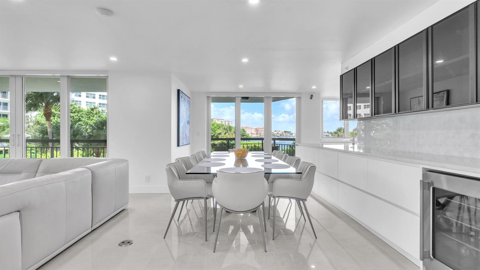 A modern dining area features a glass table, white chairs, and a sleek kitchen — 901 E Camino Real # 2a, Boca Raton FL 33432, BOCA RATON, FL