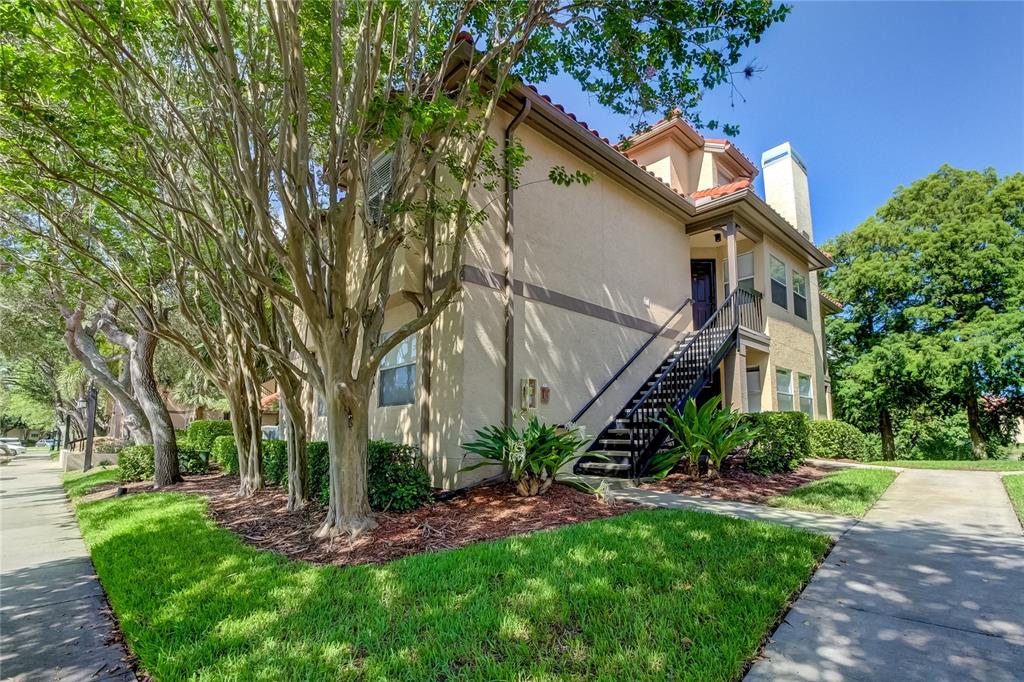 A two-story apartment building with tan stucco walls, a black metal staircase, and landscaping — 2400 FEATHER SOUND DRIVE UNIT 1228, CLEARWATER, FL