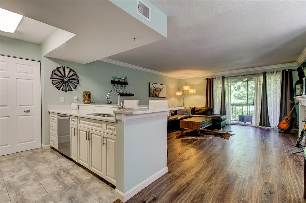 A kitchen with white cabinets and a breakfast bar opens into a living room area — 2400 FEATHER SOUND DRIVE UNIT 1228, CLEARWATER, FL