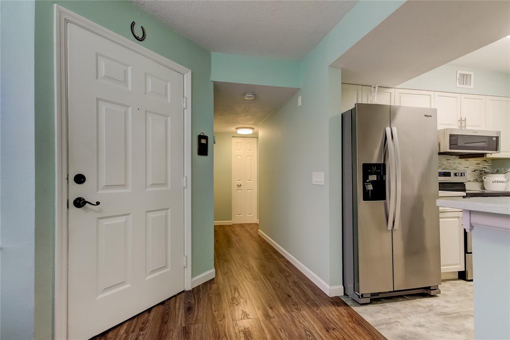 A hallway with wood-look flooring connects a white entry door to a kitchen with stainless appliances — 2400 FEATHER SOUND DRIVE UNIT 1228, CLEARWATER, FL
