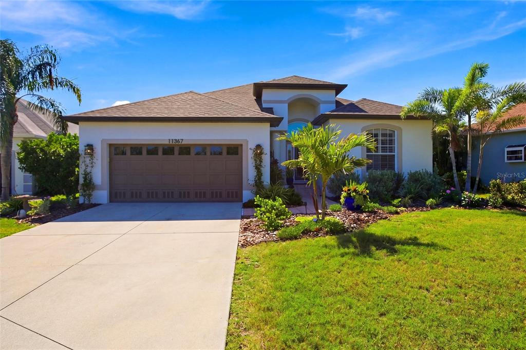 A single-story house with a brown garage door, palm trees, and a green lawn — 11367 PERICO ISLE CIRCLE, BRADENTON, FL