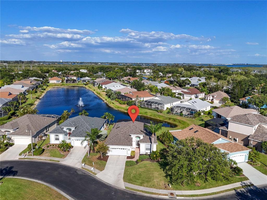 An aerial view shows a suburban house with a pool cage beside a small lake — 11367 PERICO ISLE CIRCLE, BRADENTON, FL